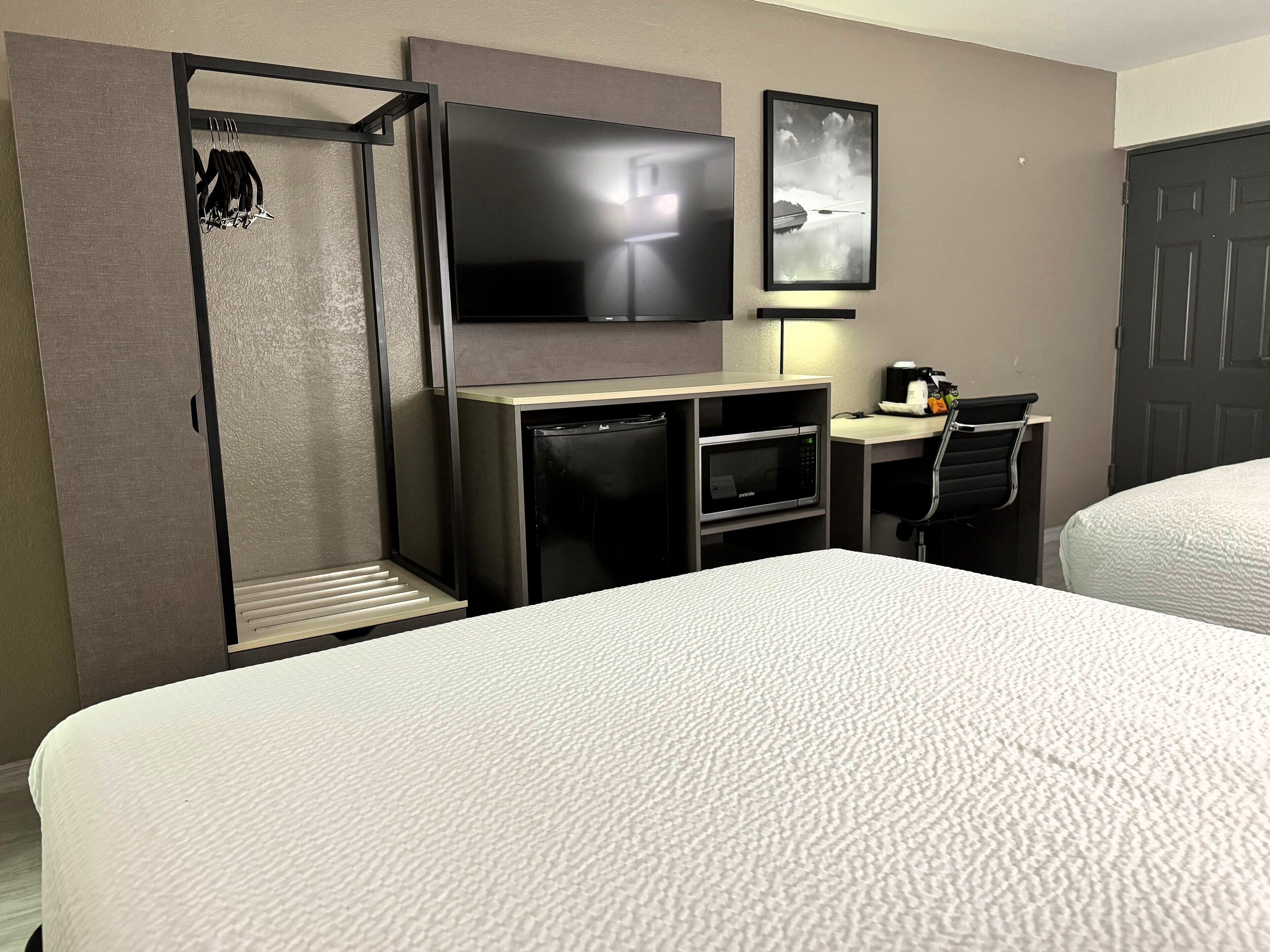 A hotel room with a bed, a TV mounted on the wall, a microwave, a desk with a chair, and a door.