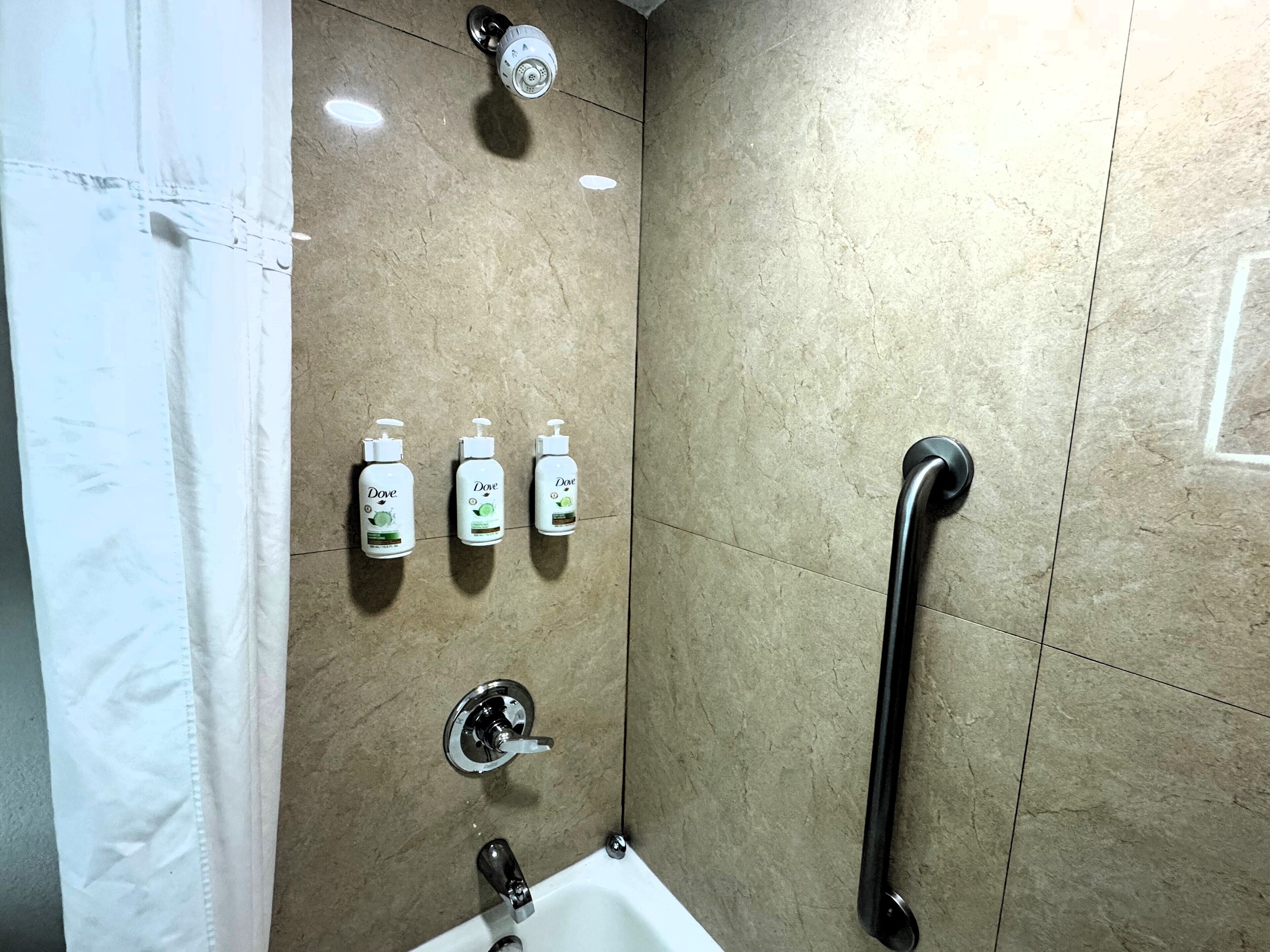 A bathroom with a shower, a handrail, and three Dove hand soap dispensers.