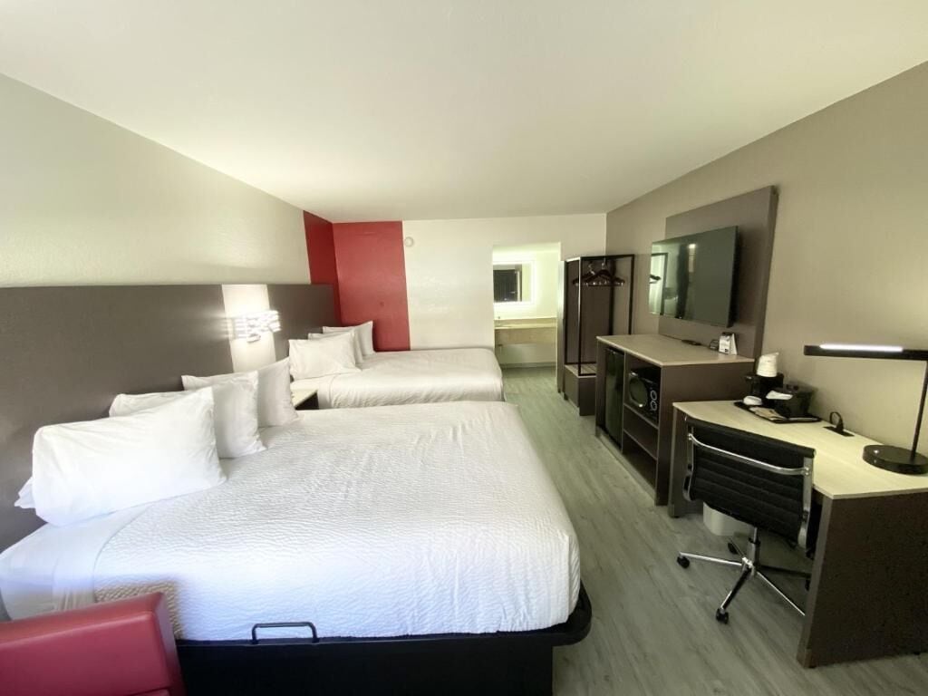 Habitación de hotel con dos camas, un escritorio con silla, televisor y refrigerador.