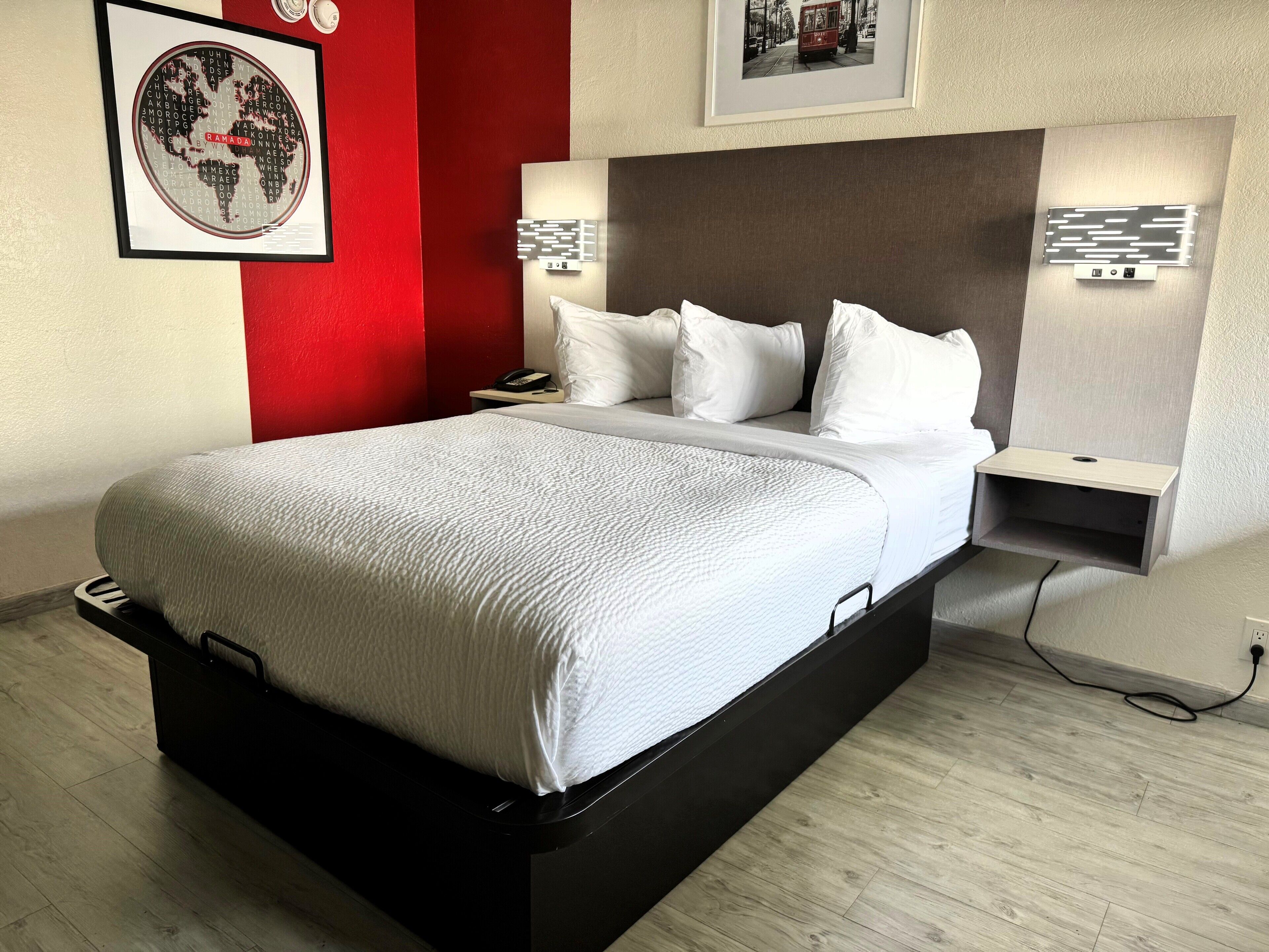Una habitación de hotel moderna con una cama grande, una pared de acento roja y una obra de arte con un mapa del mundo.