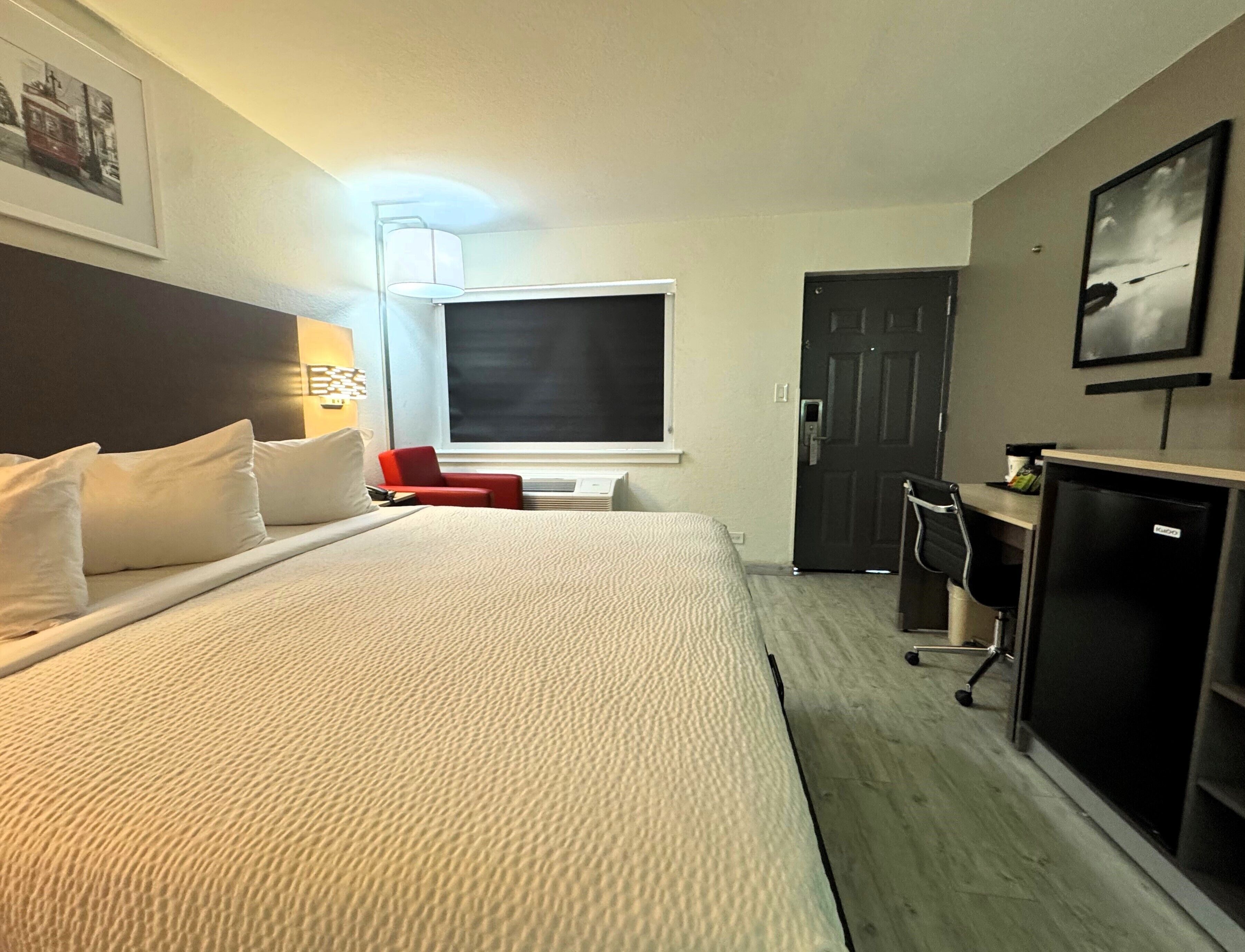 A hotel room with a large bed, a TV, a desk, and a door.