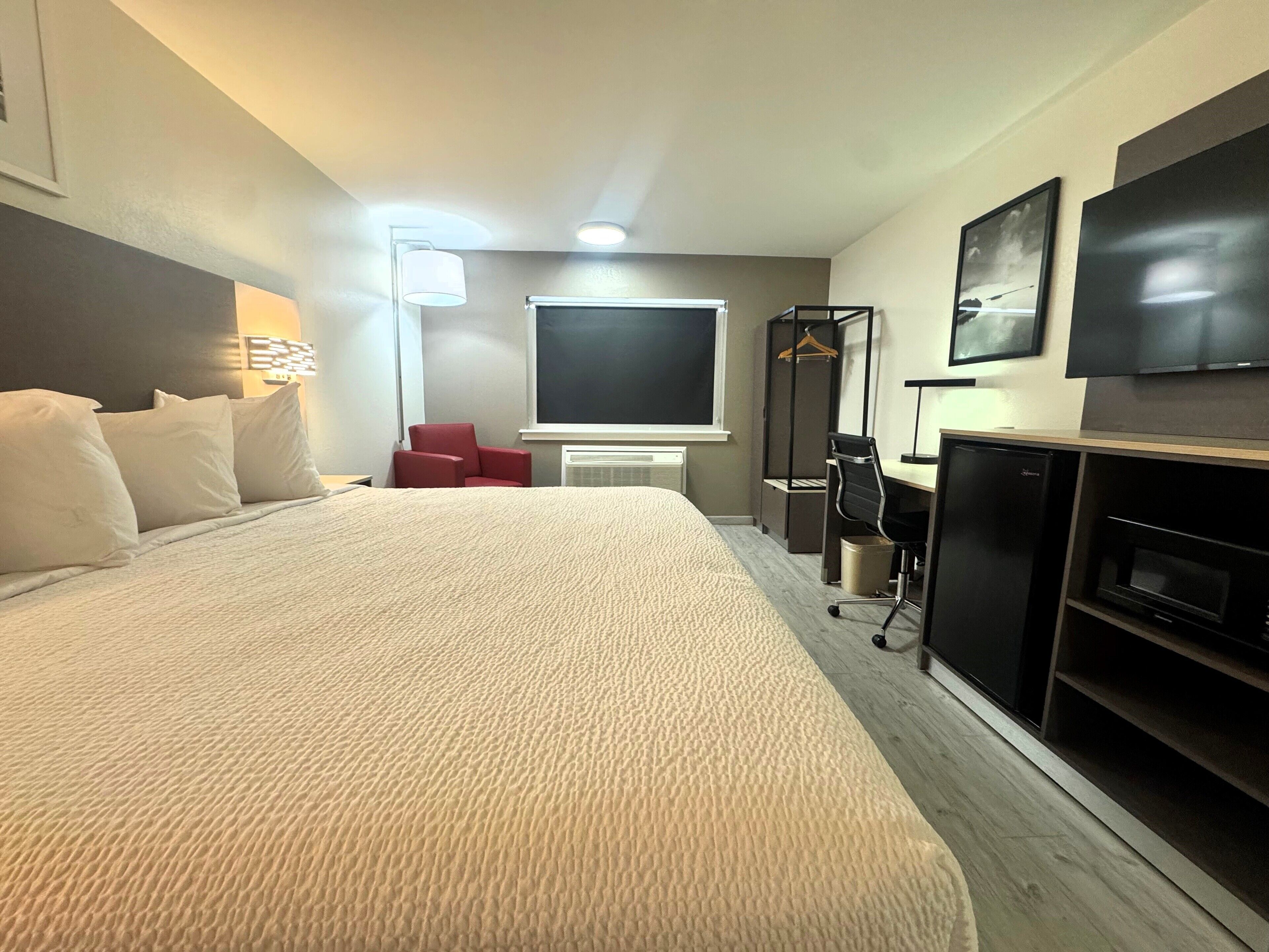Quarto de hotel com uma cama grande, escrivaninha, cadeira, televisão e aquecedor.