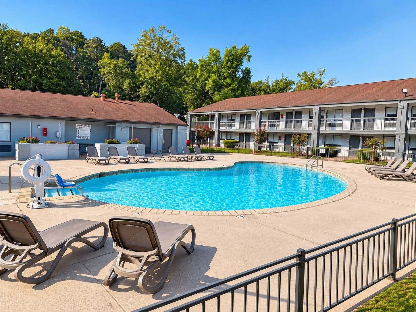A swimming pool with lounge chairs, a lifeguard stand, and a building with multiple balconies.