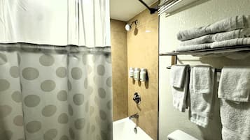 Een badkamer met douchegordijn, bad, toilet en een handdoekrek met handdoeken.