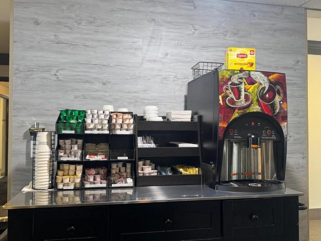 A coffee station with a coffee machine, various coffee pods, and disposable cups.