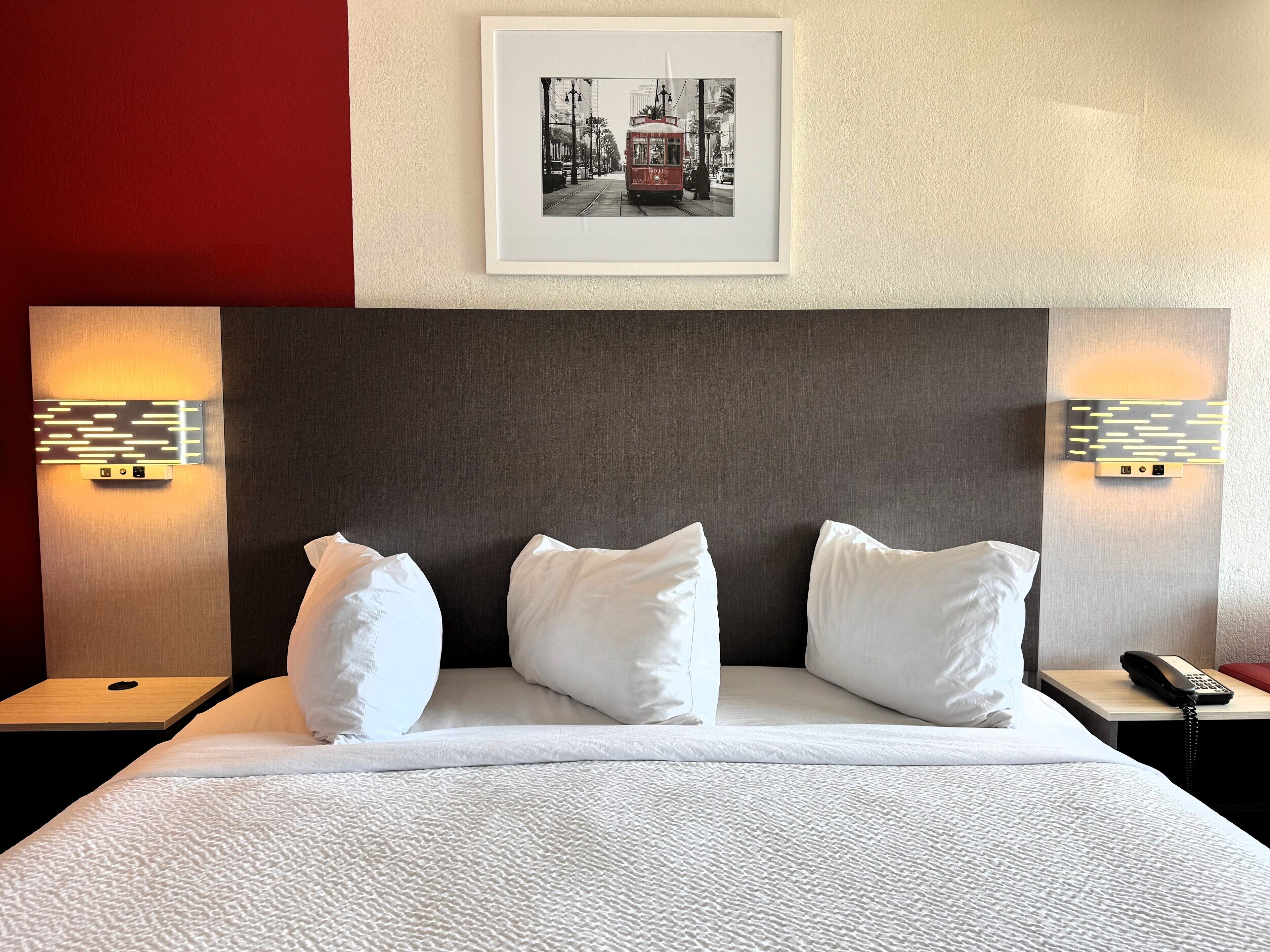 A hotel room with a large bed, white bedding, and a framed picture on the wall.