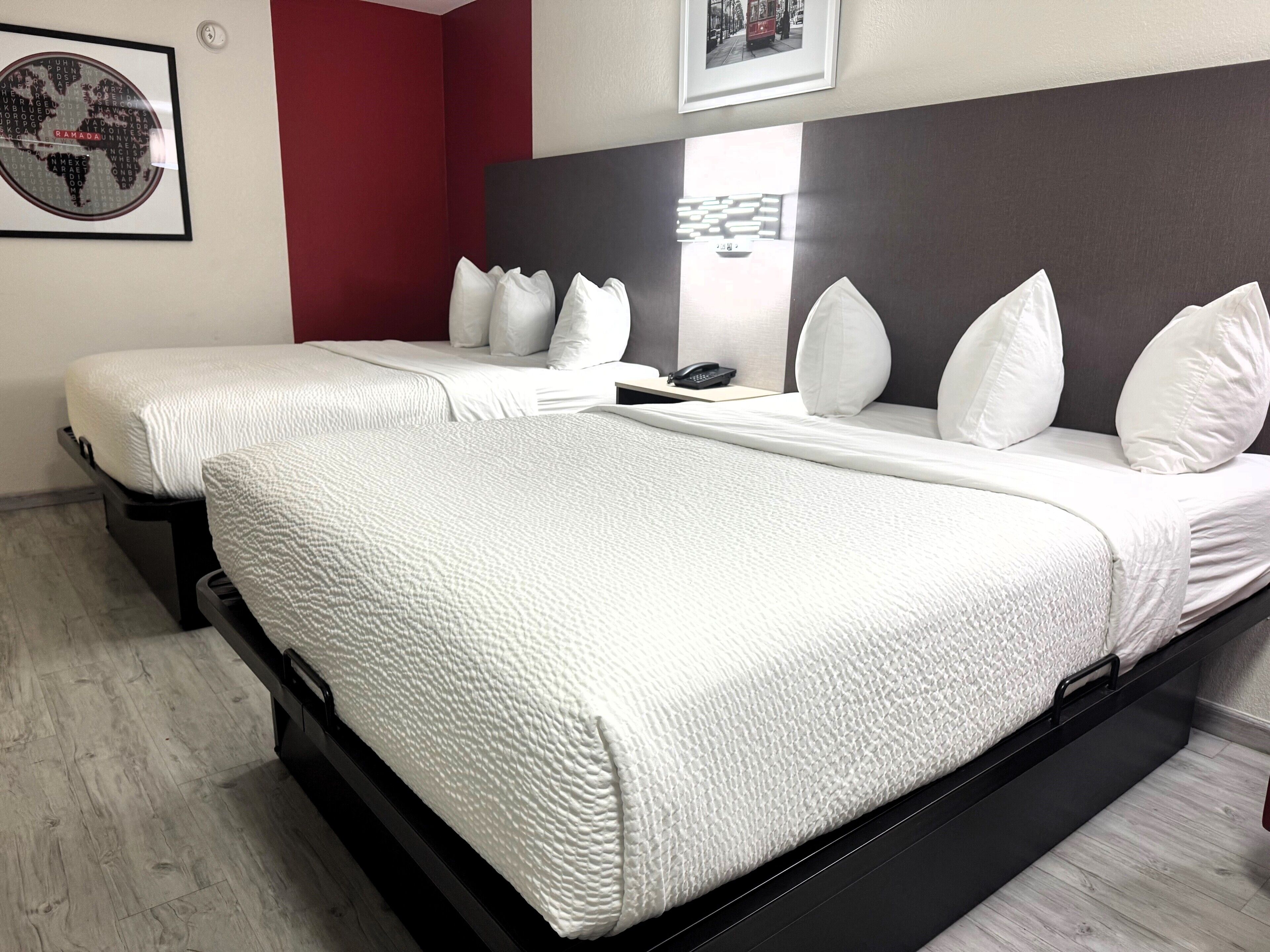 Habitación de hotel con dos camas, una pared de acento roja y una obra de arte con un mapa del mundo.