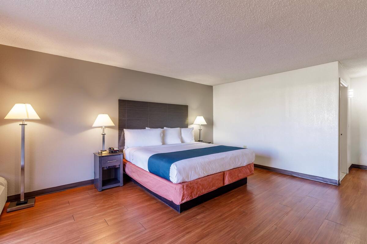 A hotel room with a bed, nightstands, lamps, and a wooden floor.