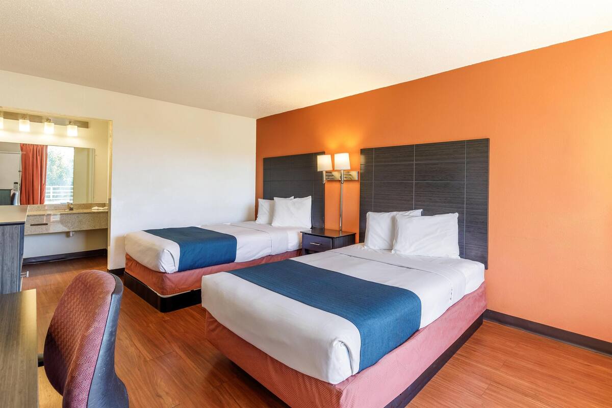 A hotel room with two beds, a desk, and a chair.