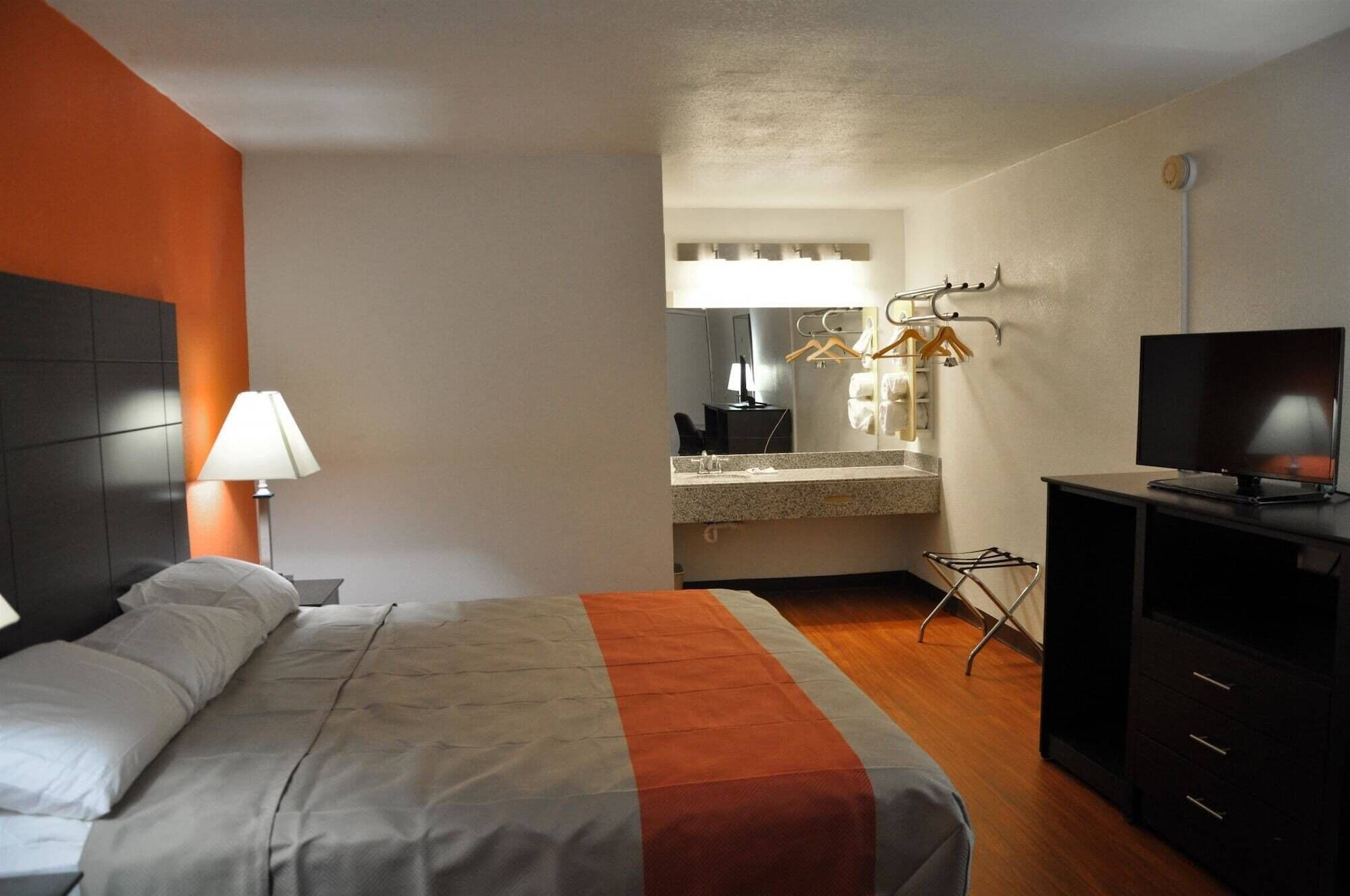 Una camera d'albergo con un letto, una scrivania, una TV e un bagno visibile attraverso una porta aperta.