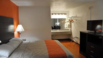A hotel room with a bed, a desk, a TV, and a bathroom visible through an open door.