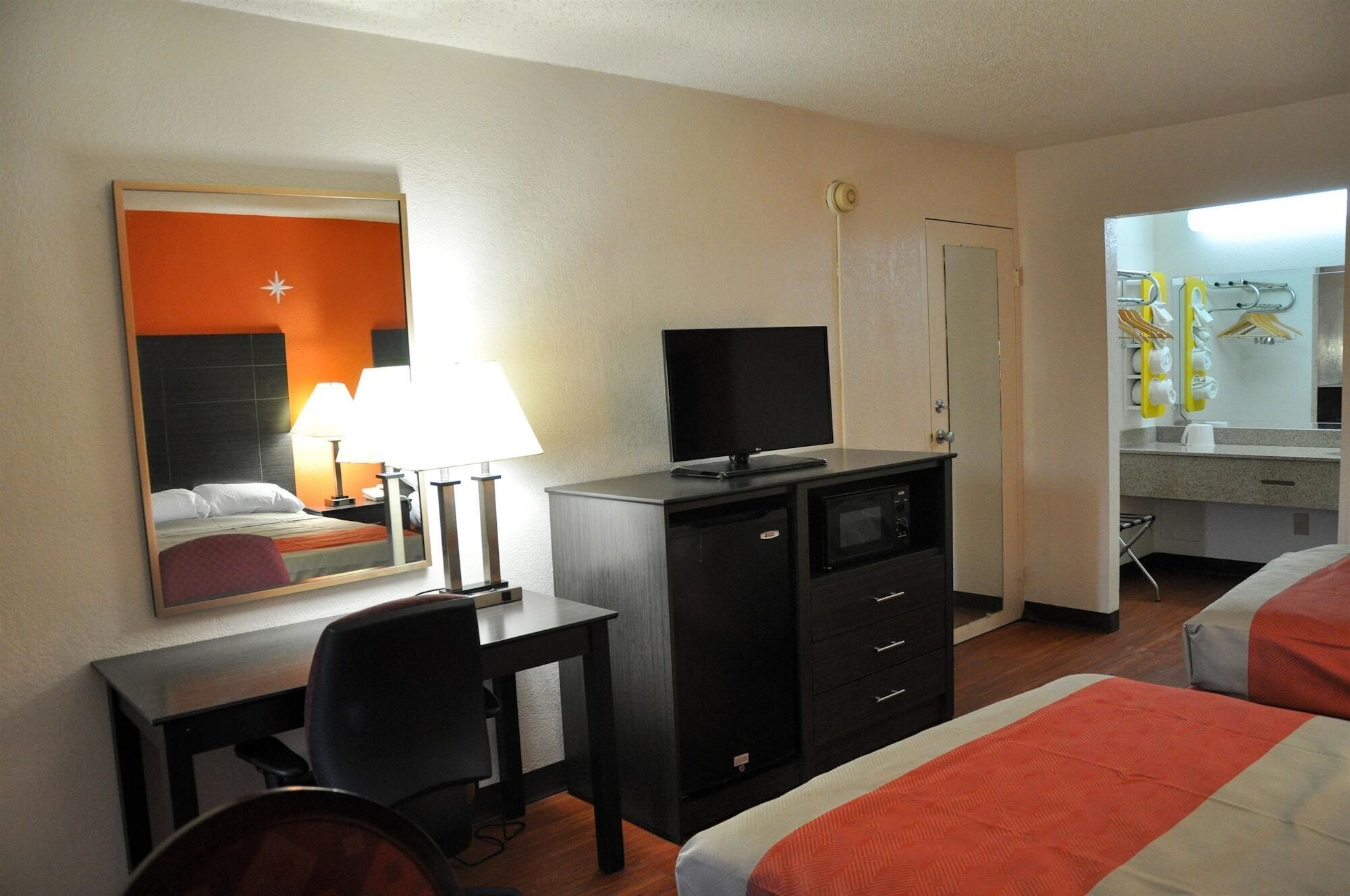 Une chambre d’hôtel équipée d’un lit, d’un bureau, d’une chaise, d’une télévision, d’un mini-bar et d’un miroir.