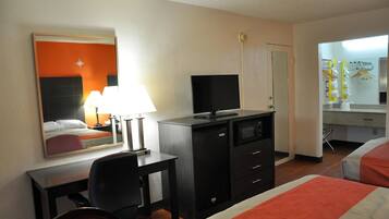 Une chambre d’hôtel équipée d’un lit, d’un bureau, d’une chaise, d’une télévision, d’un mini-bar et d’un miroir.