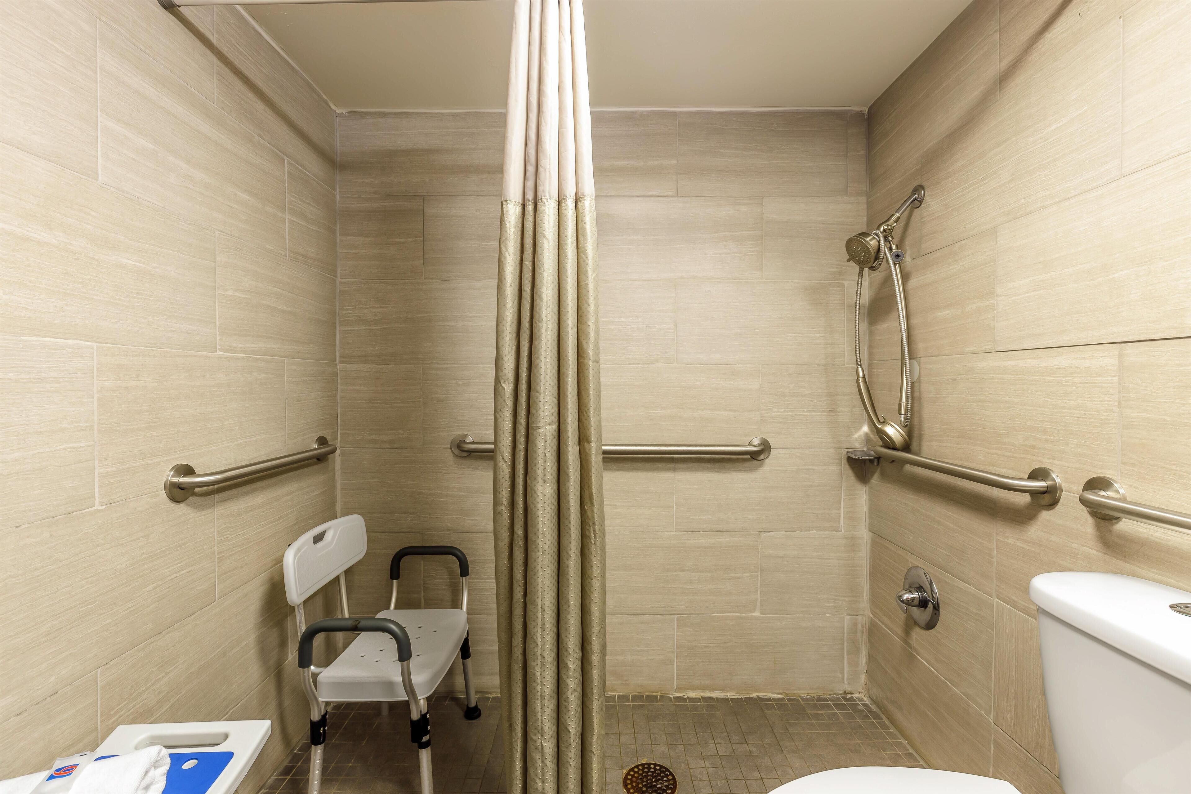 A wheelchair-accessible shower stall with grab bars, a toilet, and a chair.