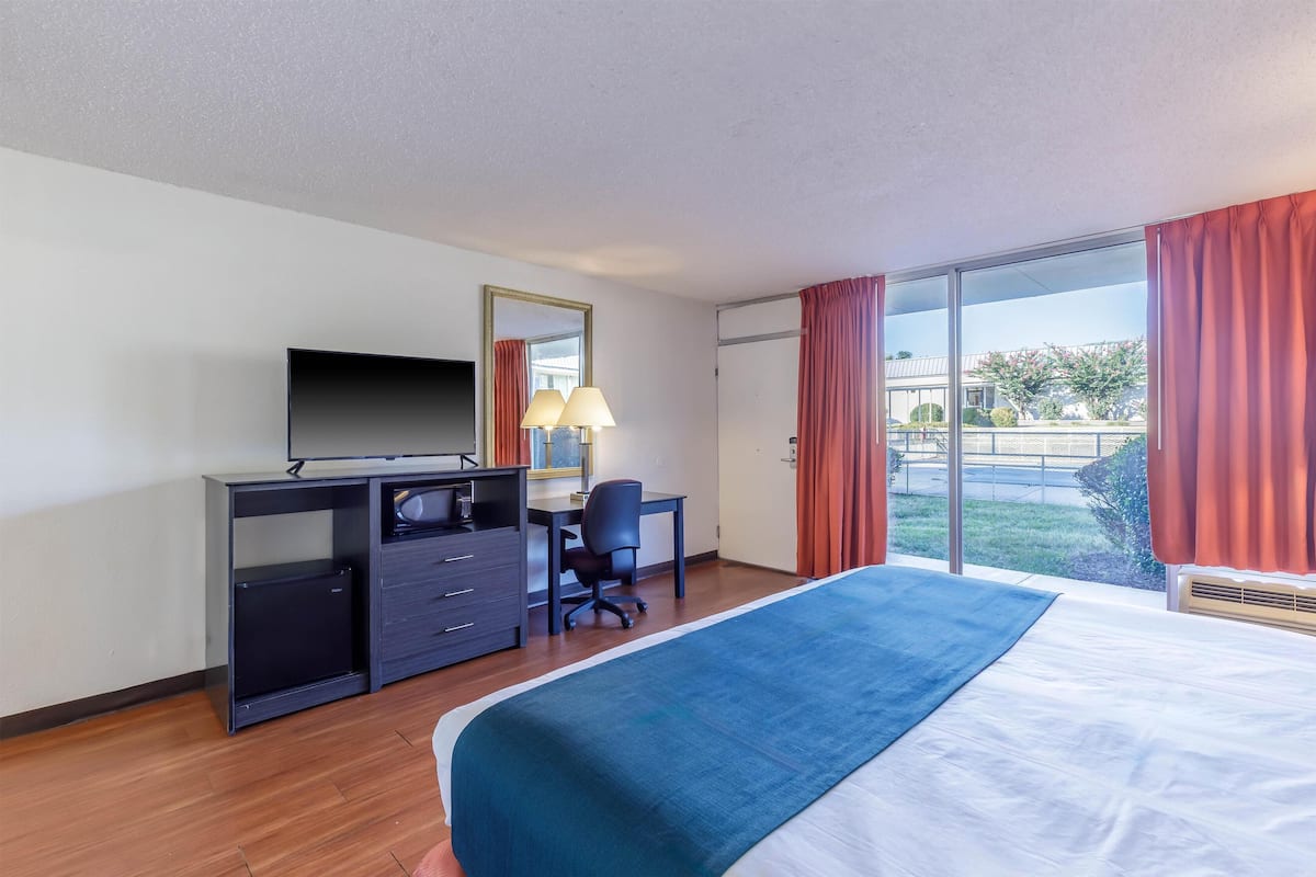 A hotel room with a bed, a desk, a chair, a TV, and a window with curtains.
