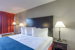 A hotel room with a large bed, two bedside tables with lamps, a heater, and a window with red curtains. - Motel 6 Dumfries, VA (Dumfries)