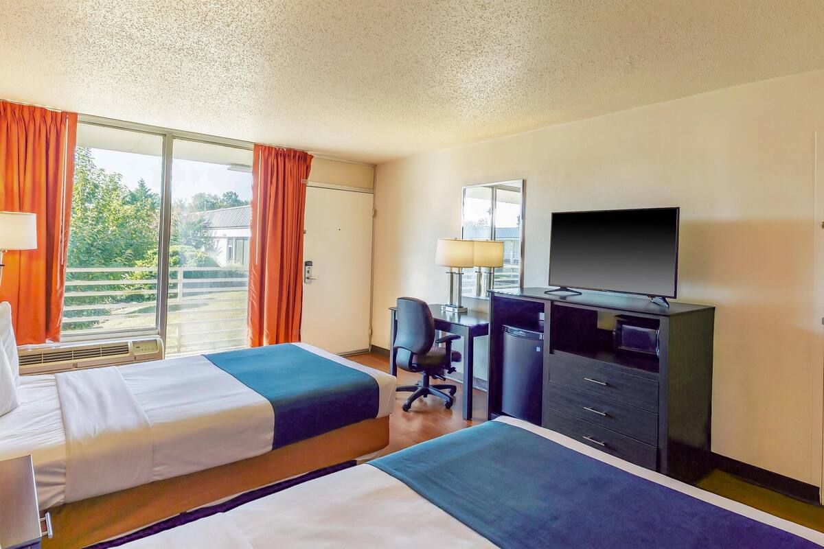 A hotel room with two beds, a desk with a chair, a television, and a wardrobe.