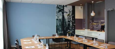 Un salón de conferencias con largas mesas, sillas, botellas de agua y documentos.