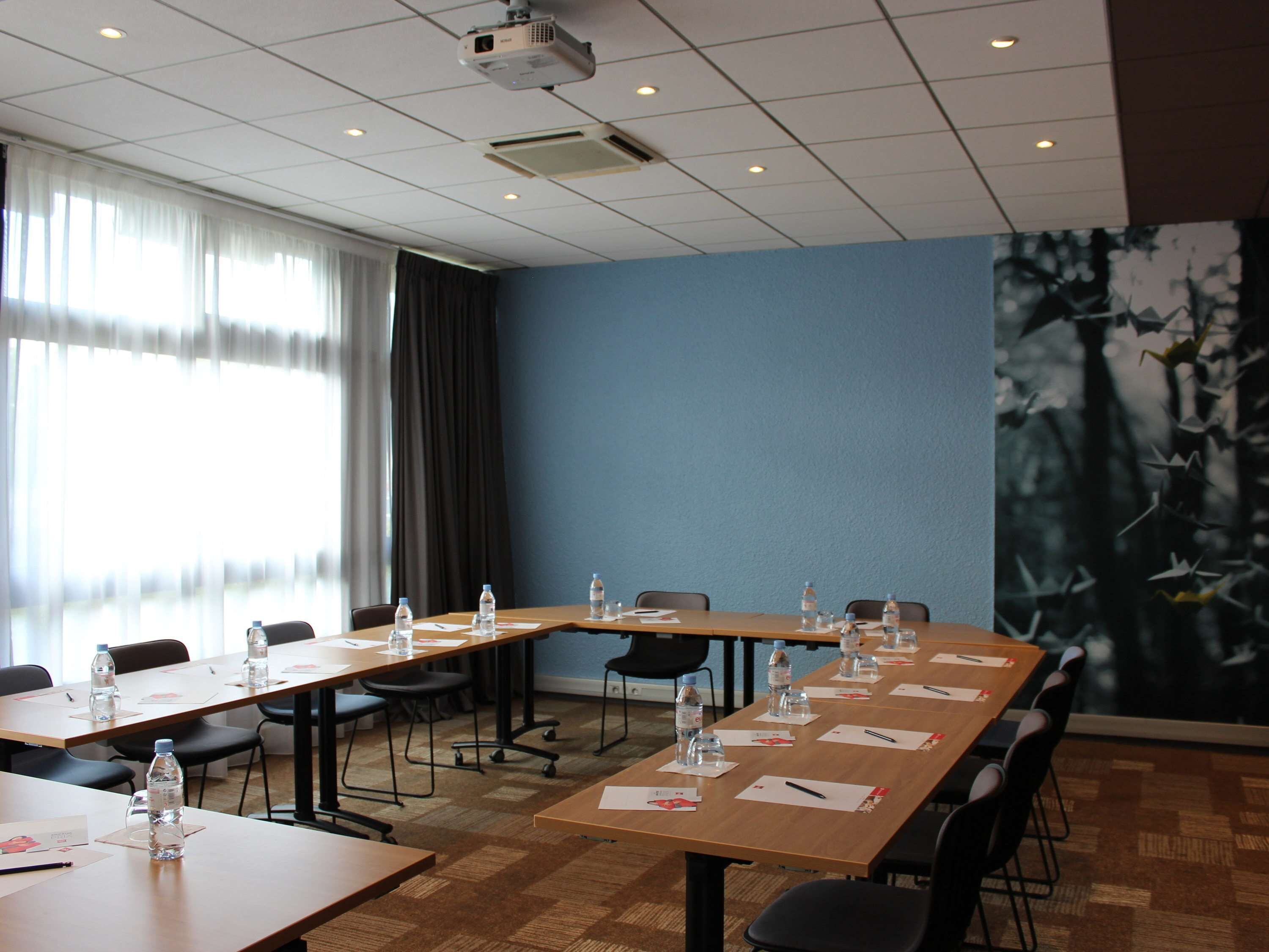Une salle de conférence avec de longues tables, des chaises, des bouteilles d’eau et des porte-noms.