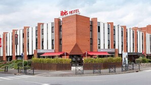 Un hotel moderno con una facciata prominente rosso e bianco, caratterizzato da un ingresso centrale con tenda rossa e un cartello che indica 'ibis kitchen restaurant'.