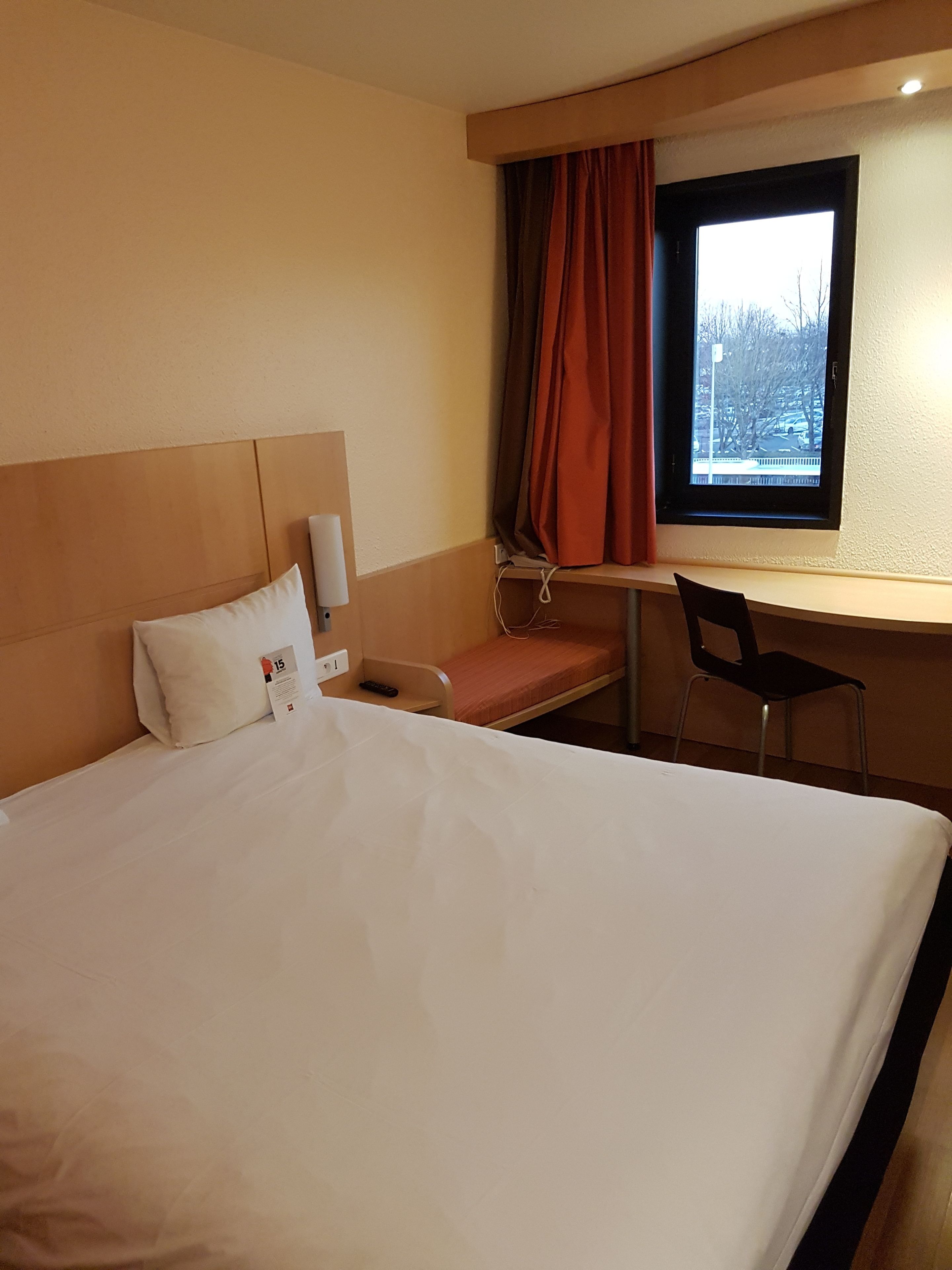 Une chambre d’hôtel avec un lit, un bureau, une chaise et une fenêtre avec des rideaux.