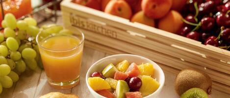 Un desayuno con un tazón de ensalada de frutas, un vaso de jugo de naranja y una variedad de frutas frescas como uvas, cerezas y kiwi.