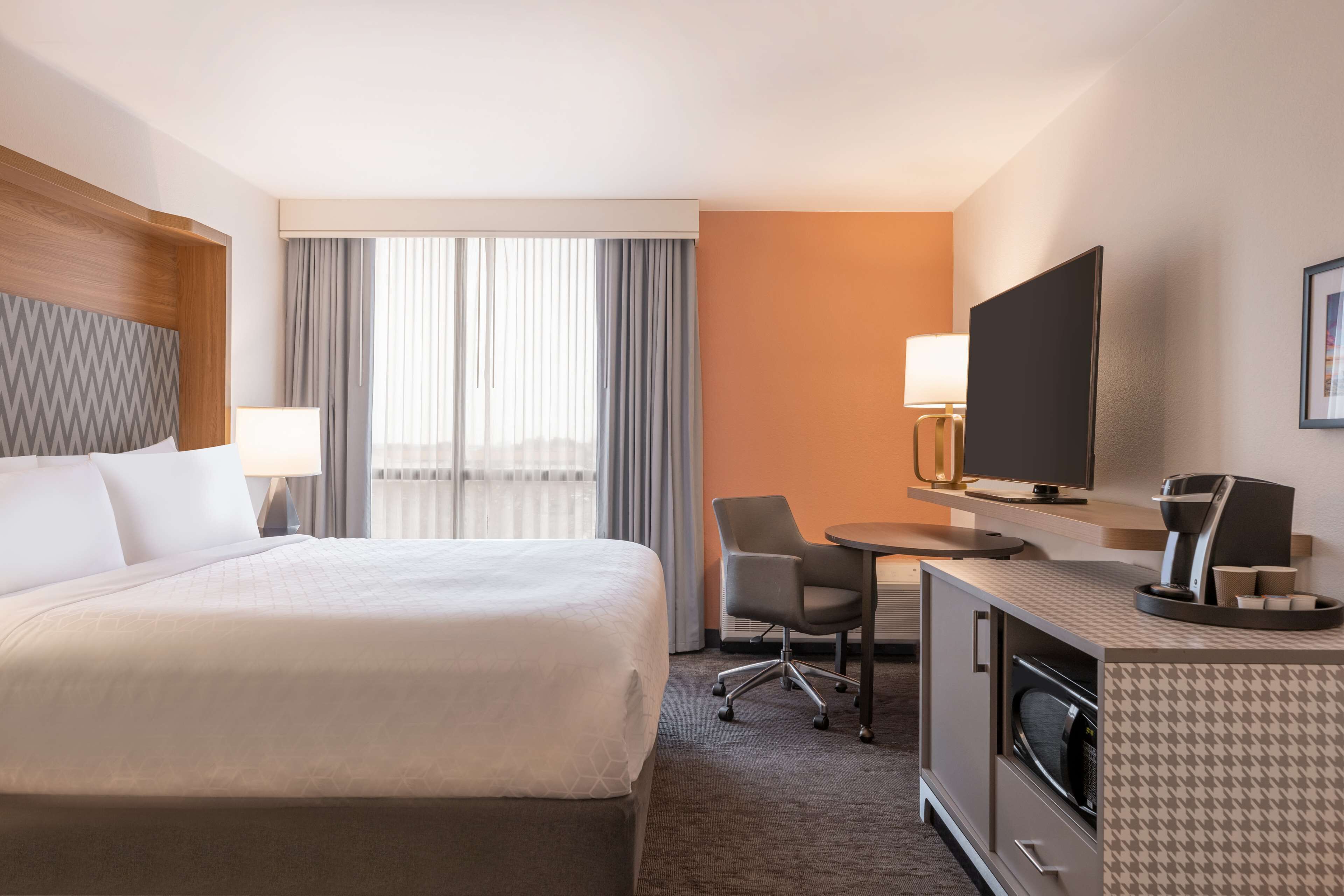 A hotel room with a large bed, a desk with a chair, a television, and a coffee maker.