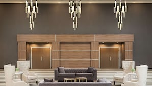 Un vestíbulo moderno con un sofá gris, dos sillones y una mesa de centro. Se observan paredes revestidas de madera y un armario grande al fondo.