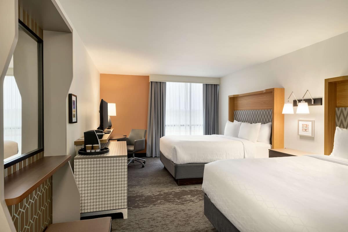A hotel room with two beds, a desk with a computer, a chair, and a large window with curtains.