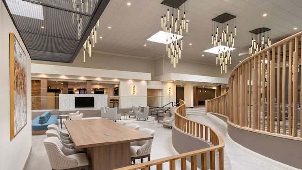 Un vestíbulo espacioso con una escalera de madera, una gran mesa de madera y luminarias modernas.