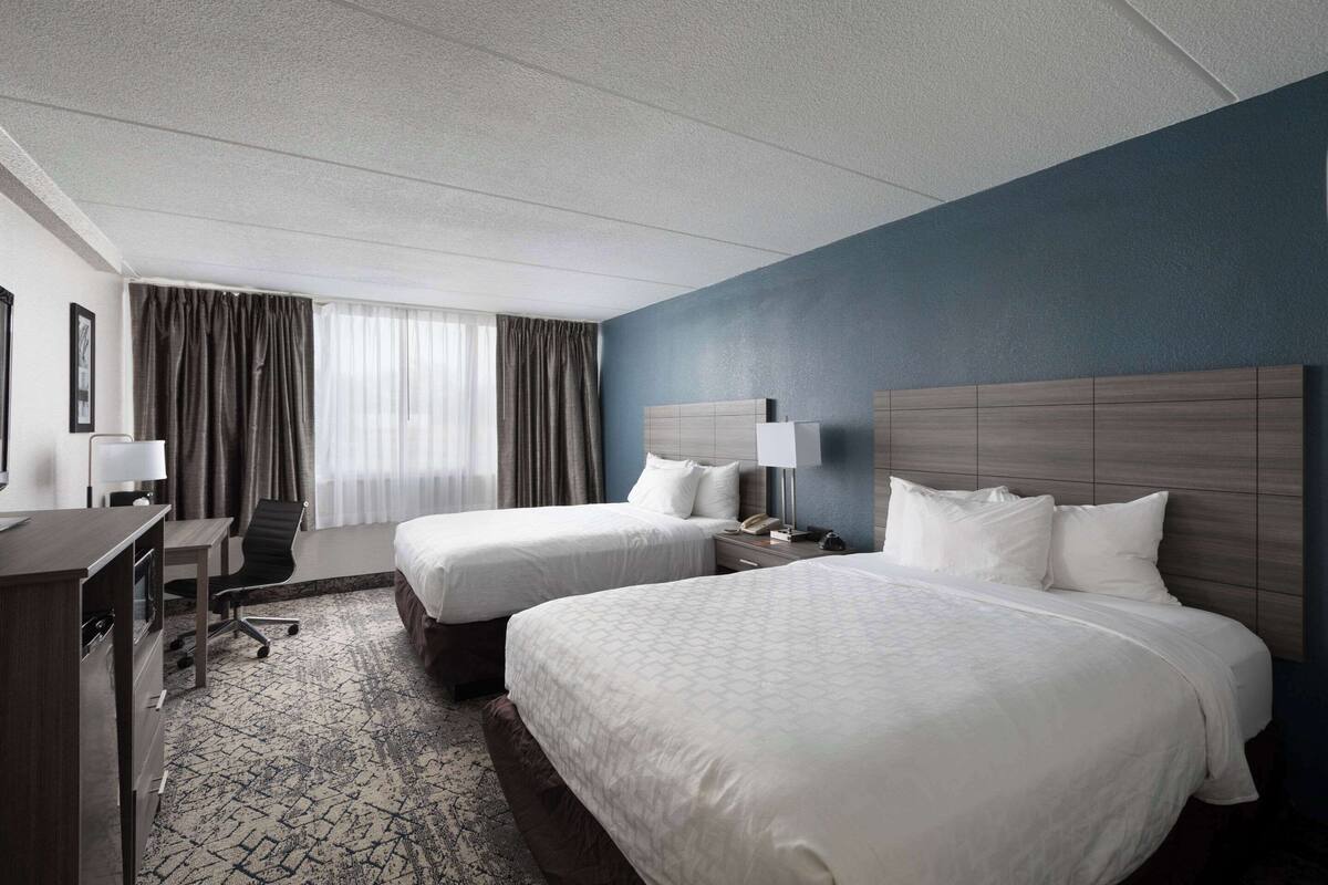 Una habitación de hotel con dos camas, un escritorio, una silla y un aparador.