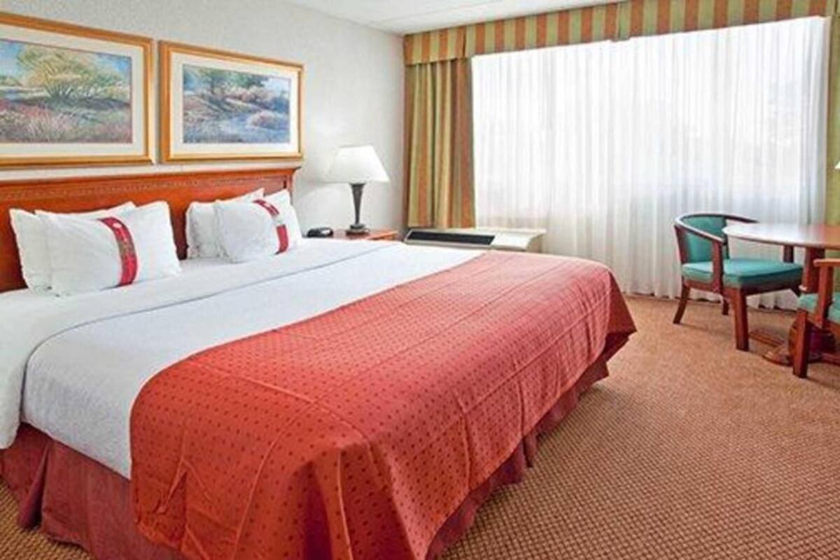 Una habitación de hotel con una cama grande, un escritorio, una silla y dos cuadros en la pared.