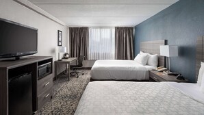 Une chambre d’hôtel avec deux lits, une télévision, un bureau avec une chaise, un four à micro-ondes et un téléphone.
