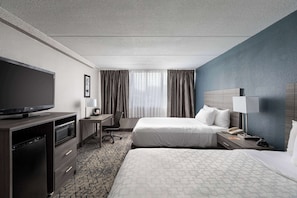 Habitación de hotel con dos camas, televisor, escritorio con silla, microondas y teléfono.