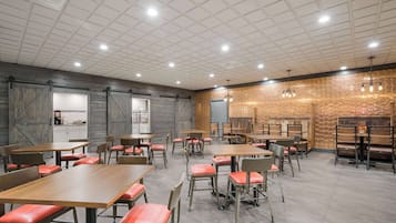 Un comedor amplio con varias mesas y sillas, una zona de cocina y una pared decorativa con un diseño estampado.