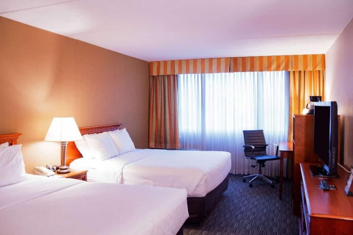 Una habitación de hotel con dos camas, un escritorio con computadora, una silla y un televisor.