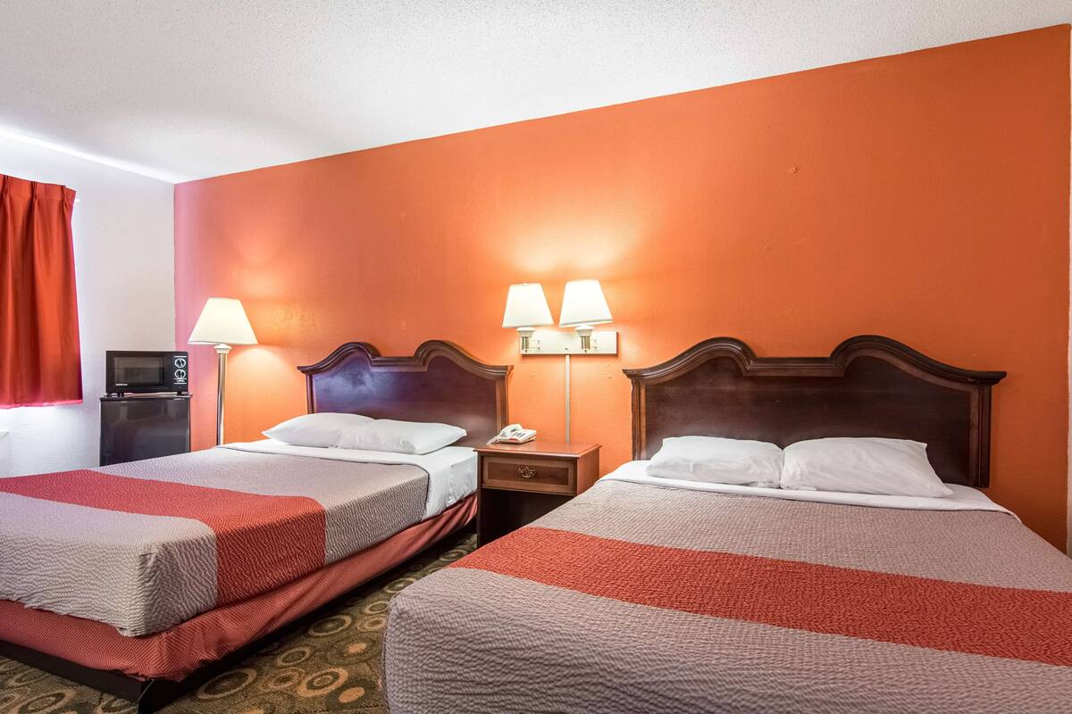 A hotel room with two beds, each with a red and white striped bedspread, a wooden headboard, and a nightstand with a lamp.