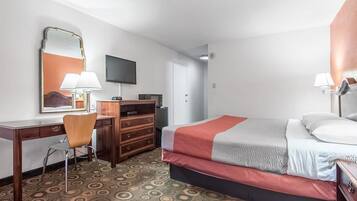 A hotel room with a bed, a desk with a chair, a dresser, a television, and a patterned carpet.