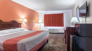 Una camera d'albergo con un letto, una televisione, una scrivania, una lampada e un condizionatore d'aria.