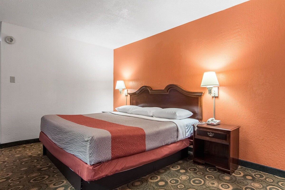 A hotel room with a bed, two bedside lamps, a telephone, and a patterned carpet.