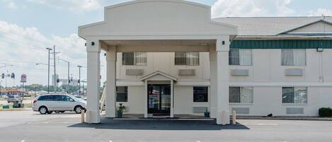 Um motel térreo com entrada central, área de estacionamento coberta e um aviso visível para um restaurante próximo.