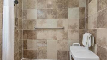 A shower area with a handrail, a white toilet, and a towel hanging on the wall.