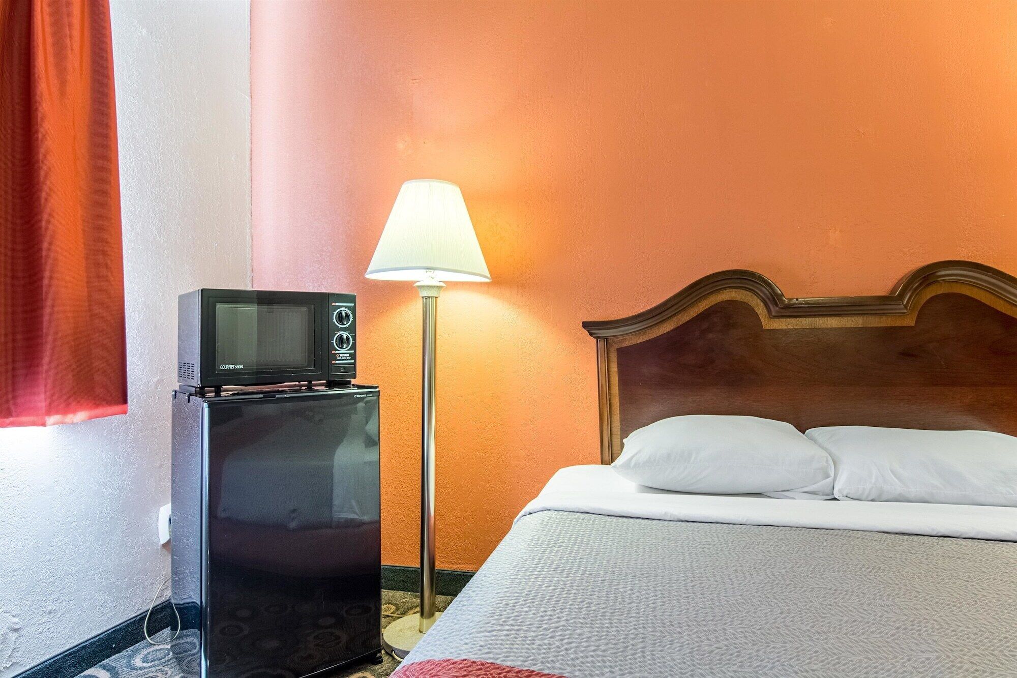 Een hotelkamer met een bed, een lamp en een kleine, zwarte koelkast met een televisie erboven.
