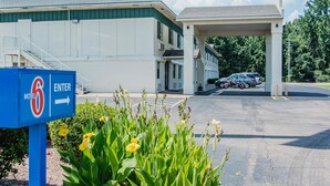 Un motel con un'area di parcheggio coperta, un segnale che indica l'ingresso e una fila di auto parcheggiate.