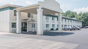 Un motel con ingresso coperto, diversi posti auto e una fila di macchine parcheggiate.