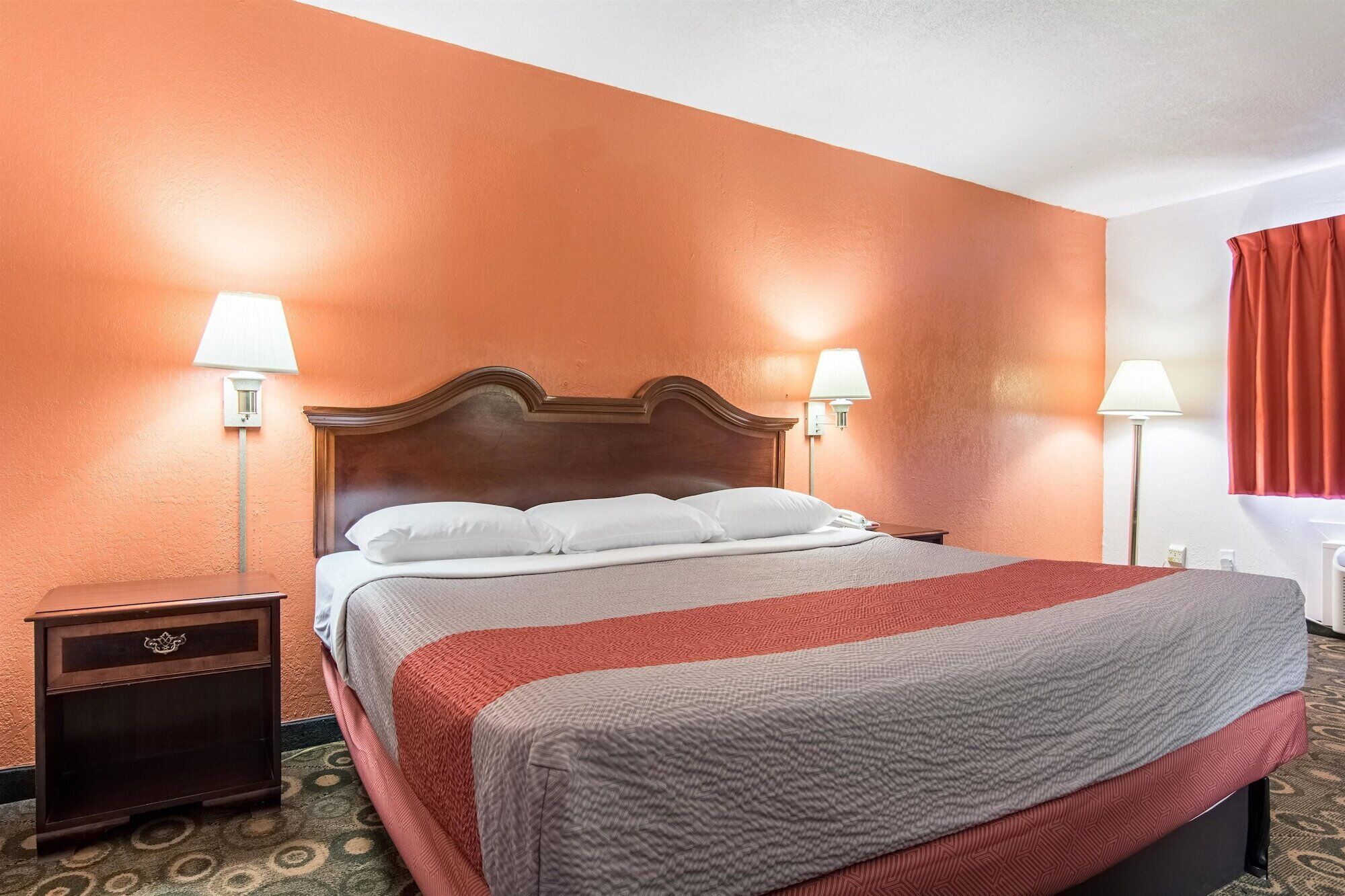 A hotel room with a bed, two bedside lamps, a nightstand, and a red curtain.