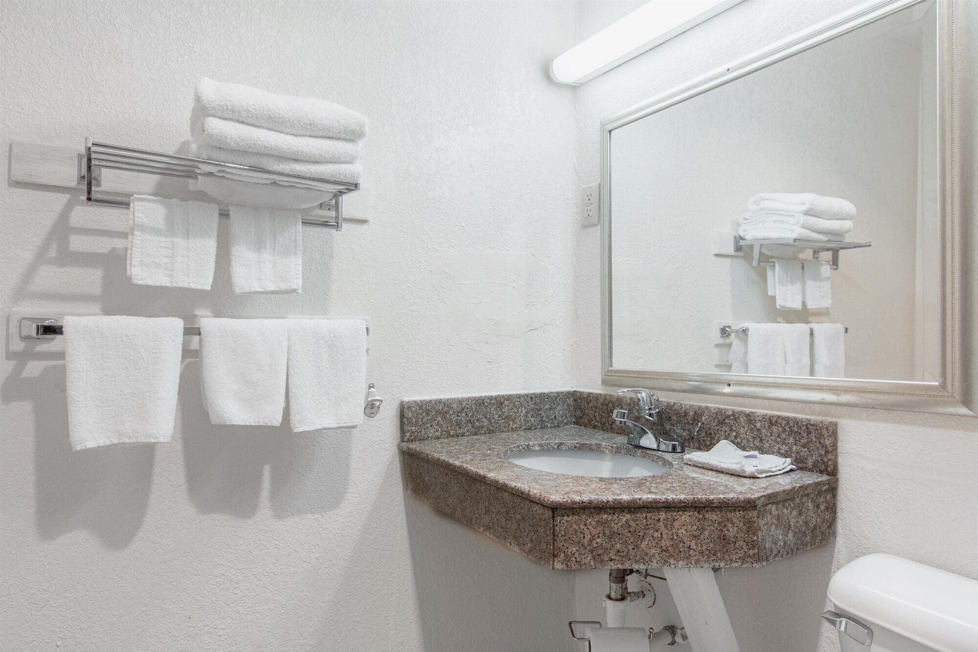 Baño con lavamanos de granito, toallas blancas y espejo.