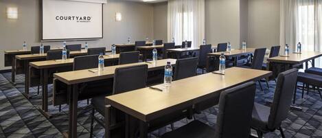 A conference room with multiple tables, chairs, and a large screen displaying "COURTYARD BY MARRIOTT".