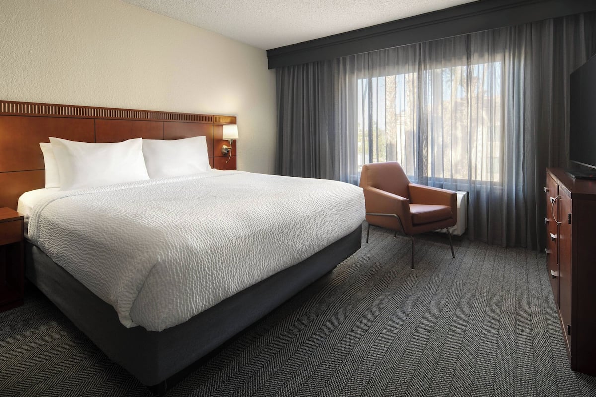 Ein Hotelzimmer mit einem großen Bett, einem Sessel, einem Schreibtisch und einem Fernseher.