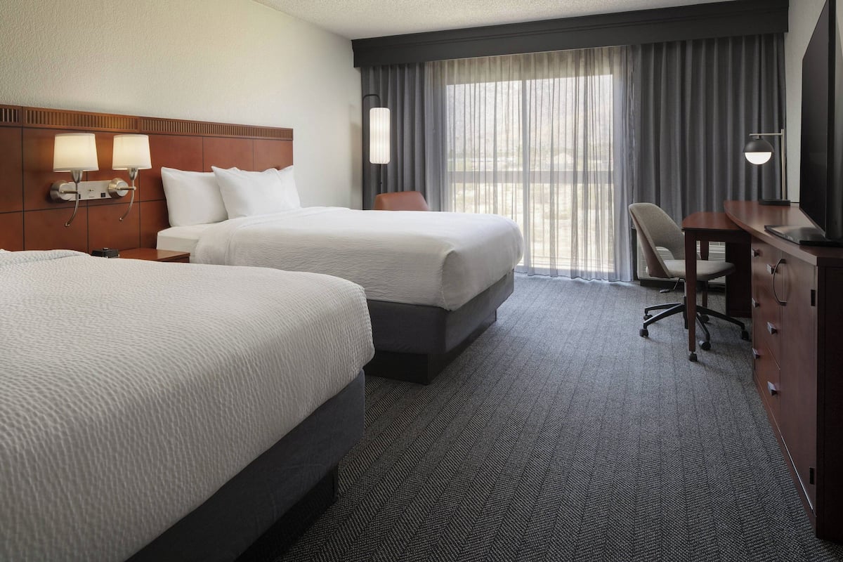Ein Hotelzimmer mit zwei Betten, einem Schreibtisch, einem Sessel und einem Fernseher.